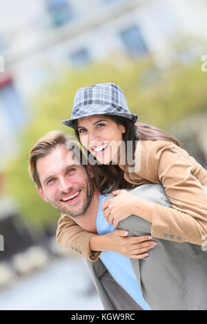 Young man giving piggyback ride to girlfriend in town Stock Photo