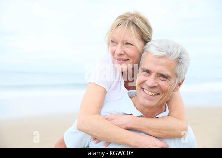 Senior man giving piggyback ride to his wife on the beach Stock Photo