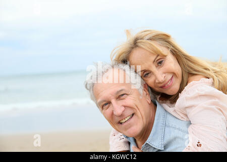 Senior man giving piggyback ride to his wife on the beach Stock Photo