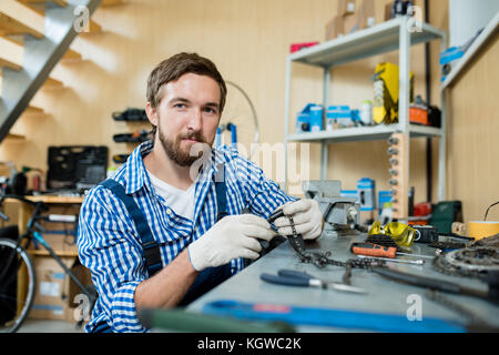 Self-employed repairman in gloves repairing chain from wheel of bicycle Stock Photo