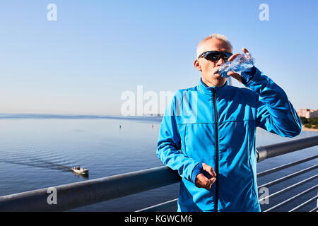 Sporty mature man drinking fresh water from plastic bottle after workout Stock Photo