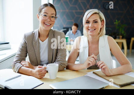 Two young successful specialists sitting by desk in office or working studio Stock Photo