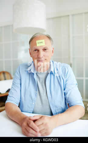 Aged man with notepaper on forehead looking at camera during leisure game Stock Photo