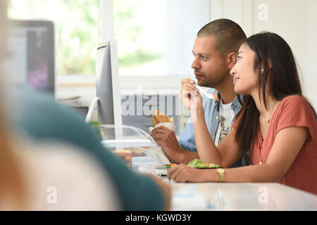Office-workers having lunch in office in front of desktop Stock Photo
