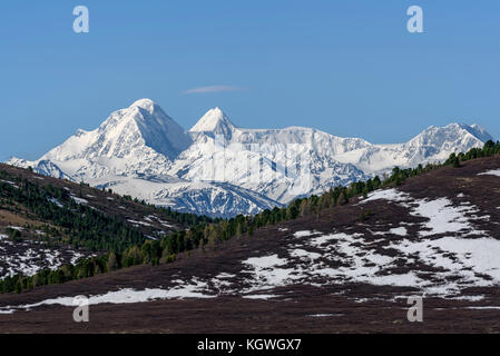 Scenic view with the beautiful mountain peaks with snow and glaciers, slopes covered with snow and sparse brown vegetation and cedar trees against a b Stock Photo