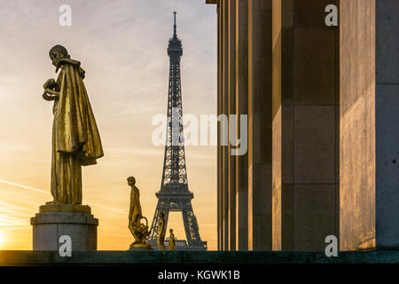 The rising sun illuminates the golden statues on the Trocadero esplanade while the Eiffel Tower stands out against an orange sky. Stock Photo