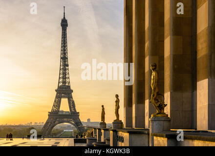 The rising sun illuminates the Trocadero esplanade and its golden statues while the Eiffel Tower stands out against an orange sky. Stock Photo