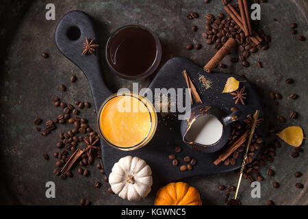 Ingredients for cook spicy pumpkin latte. Glasses with black coffee, pumpkin milk, jug of cream on black serving board. Spices, coffee beans above ove Stock Photo