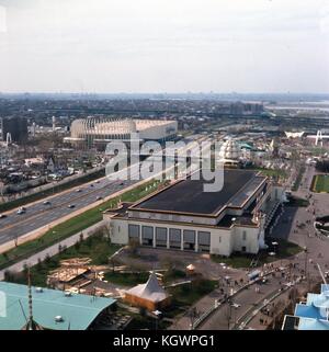 Panoramic aerial view facing northwest across the 1964 New York World's Fairgrounds toward LaGuardia Airport on Flushing Bay, in Corona, Queens, New York, May, 1964. The Wisconsin Pavilion is in the lower left corner along the Avenue of The States. New York City Pavilion and Ice Theater building is at center frame, with Hollywood USA and the balloon-shaped Brass Rail restaurant seen behind. To the left of the NYC building running north-south is the Grand Central Parkway. At center frame spanning the highway is the Bridge of the United Nations North. Across the road along the southbound highway Stock Photo