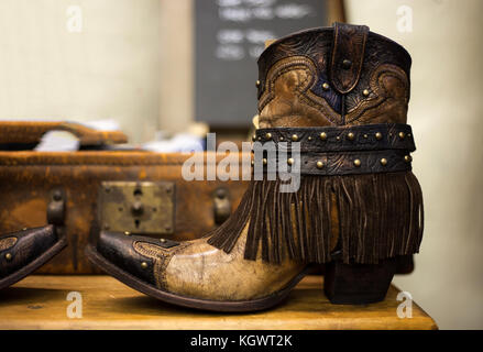 Pair of handmade brown leather cowgirl boots with vintage suitcase in background Stock Photo