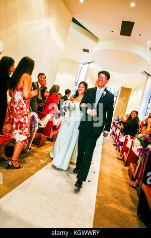 Beaming bride and groom walking out of church after wedding ceremony with people cheering on Stock Photo