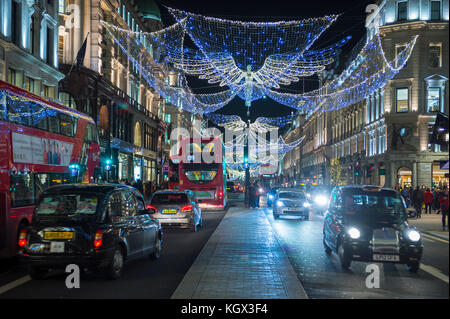LONDON - NOVEMBER 18, 2016: Red double-decker buses pass under twinkling Christmas angels lighting up the upscale shopping district of Regent Street. Stock Photo