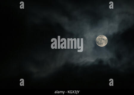 A full moon behind the clouds during the cloudy night. It is hiding and is visible only for few seconds. Stock Photo