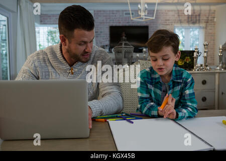 Father assisting son in his studies at table Stock Photo