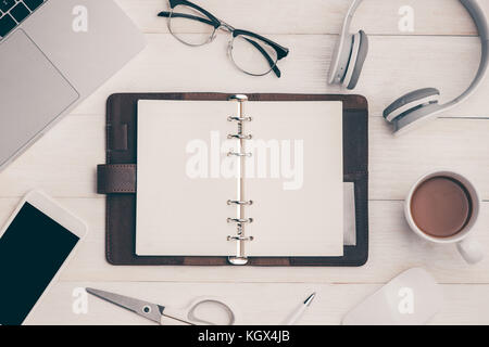 Top view on opened notebook, smartphone, laptop, eyeglasses, cup of coffee and other equipment on wooden office desk. Stock Photo