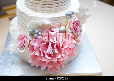 Close-up photo of white sugar coated tree layered wedding cake with focus on pink decorative edible marzipan flowers placed on the side of a cake Stock Photo