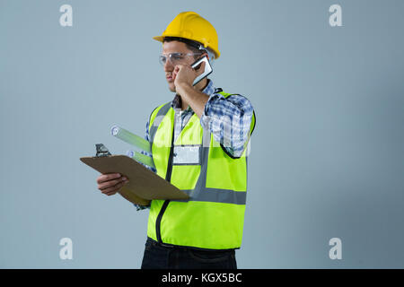 Male architect holding clipboard and talking on mobile phone against white background Stock Photo