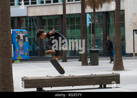 A young male Australian skateboard rider performs a flip or ollie over a timber bench in Sydney city, Australia Stock Photo