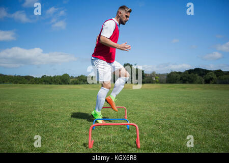 Soccer player practicing on obstacle in ground Stock Photo