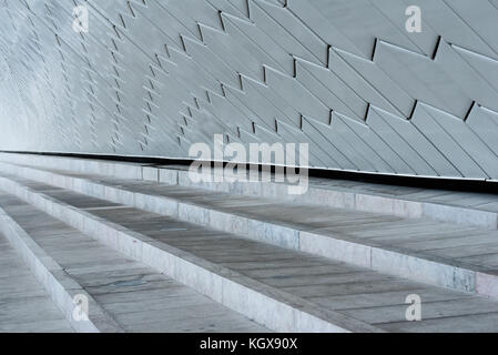 Detail of stone steps running along the length of an exterior white curved ceramic brick wall Stock Photo