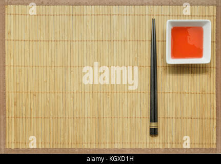 Black Wooden chopsticks and sweet and sour sauce on bamboo mat background. Stock Photo