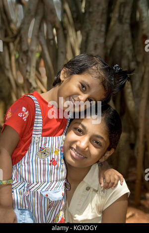 Smiling baby girl lovingly leaning over her elder sister Stock Photo