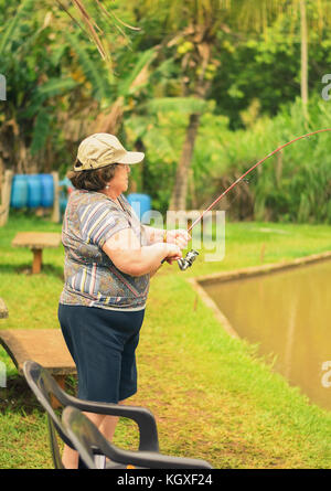 Old woman holding a fishing rod, hooking a fish on a lake. Brazilian women  descendant of japanese fishing Stock Photo - Alamy