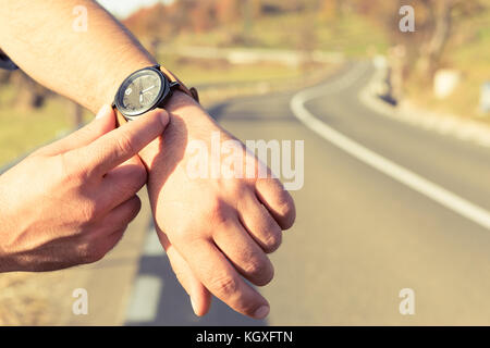 Man hands checking time on wristwatch on the road side as traveling time or waiting for the bus concept Stock Photo