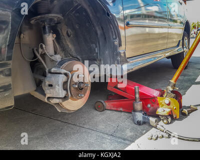 Car on jack lift with one tire removed reveal the rusty disc brake. Tire replacement on road side. Stock Photo