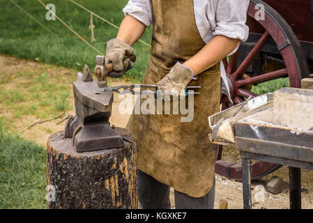 Blacksmith working on an iron object with a hammer during a workshop. Stock Photo