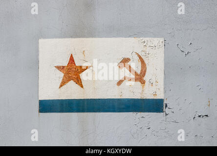 Red star and crossed hammer and sickle, communist symbols, painted in a white rectangle on a weathered, grey surface. Stock Photo
