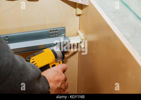 Repairman In Overalls Repairing Cabinet Hinge In kitchen cabinets Stock Photo