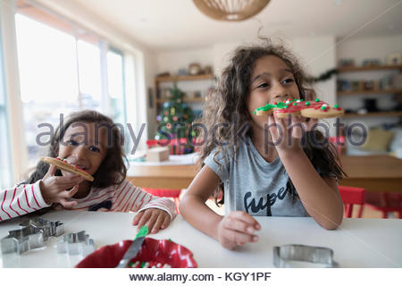 Girl sisters eating decorated Christmas gingerbread cookies in kitchen