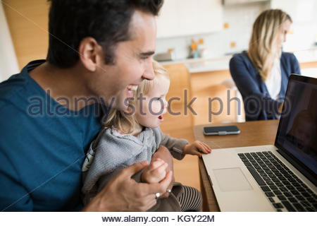 Playful father holding daughter on lap at laptop