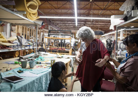 Female fashion designers fitting, pinning fabric on woman in workshop