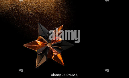 Star from black cardboard and bronze colored foil in front of black background Stock Photo