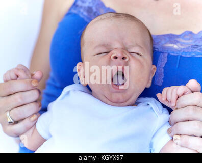 Infant baby boy in mother's arms yawning with eyes closed Stock Photo