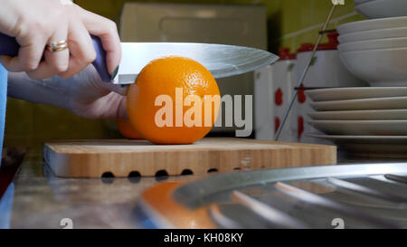 Female hands cutting orange on wooden board table in kitchen. Stock Photo