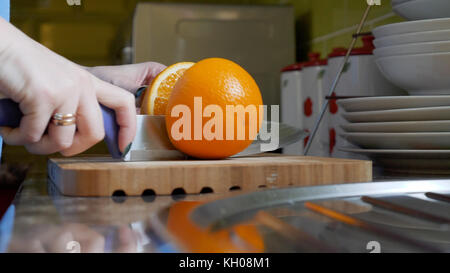 Female hands cutting orange on wooden board table in kitchen. Stock Photo