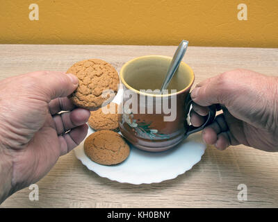 Drinking tea from mug and eating oatmeal cookies close up. Stock Photo