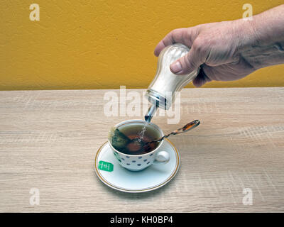 Hand with glass sugar holder pour sugar in tea cup. Stock Photo