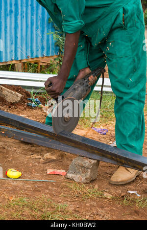African male metal worker using metal grinder to cut steel beams, Kenya, East Africa Stock Photo