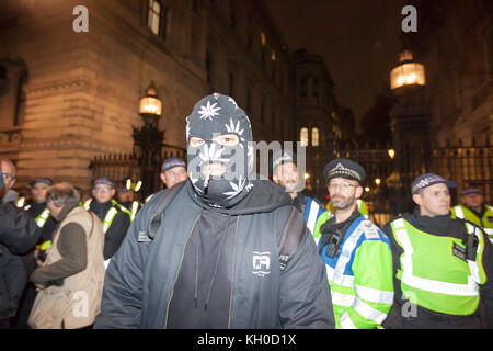 A Million Mask March activist wears a balaclava and smokes a joint in front of the police at the Million Mask March 2015 in London. Stock Photo