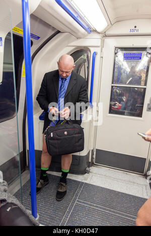 A no trousers participants is checking his smart phone in the tube as the No Pants Subway Ride in London. Stock Photo