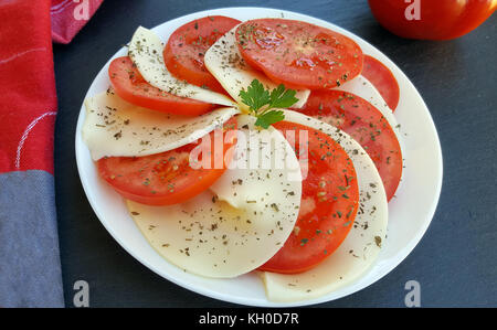 Caprese salad with ripe tomatoes and mozzarella cheese on dark stone background Stock Photo