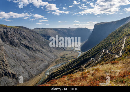 The picturesque top view on the steep winding gravel road through the pass, going up the mountain slope, the valley between the mountains and the rive Stock Photo