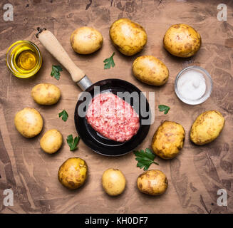 cooking homemade burger with fries, parsley and spices, beef fillet in a small pan,  on wooden rustic background top view close up Stock Photo