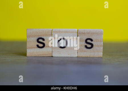 SOS word on  wood cubes on table against yellow background Stock Photo