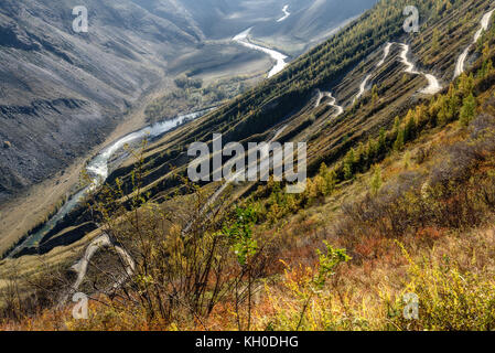 The picturesque top view on the steep winding gravel road through the pass, going up the mountain slope, the valley between the mountains and the rive Stock Photo