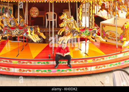 A fairground worker looks at phone sitting on a merry-go-round on Brighton seafront Stock Photo